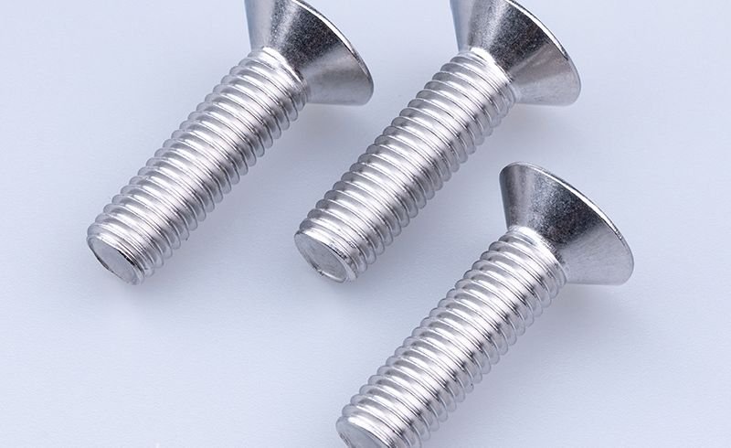 Three stainless countersunk socket screws lying on their side on a white background