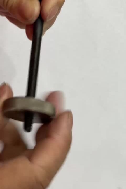 A long black threaded rod being checked with a thread ring gauge held in one hand