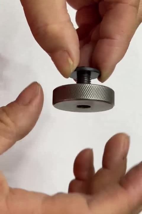 A hand holding a hex screw that has run fully through a knurled thread ring gauge